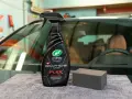 En flaska med "Graphene Flex Wax" och en svamp ligger på en grå trasa framför en bil.