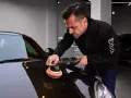 Man polerar en mörk bil med en polermaskin. Autosol ger glans åt lacken.