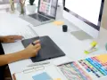En grafisk designer arbetar vid sitt skrivbord med en ritplatta, tangentbord och en färgkarta. En bra **concept vista prisjakt** för kreativa projekt.