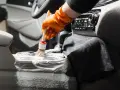 En hand med orange handske använder en **detail brush** för att rengöra bilens mittkonsol med skum.