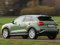 Grön Audi Q2 kör på en landsväg, med suddiga träd och fält i bakgrunden. Kanske ett audi q2 problem med att den kör för fort?