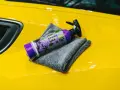 En flaska spray wax ligger på en gul bil med en grå mikrofiberduk.