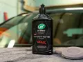 En flaska Turtle Wax Hybrid Solutions Pro Graphene Infused Wax, ett bilschampo för maximal glans och skydd, ligger på en grå handduk.