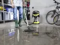 Man i gröna stövlar använder Kärcher WD 6 P Premium för att suga upp vatten på ett betonggolv i ett garage.