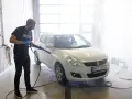Man med högtryckstvätt gör bilen skinande ren. En riktig asfaltslösare som får bort all smuts.