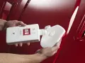 Händer applicerar Autoglym Super Resin Polish på en blank röd bil med en svamp.