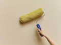 En hand håller en färgroller med gul päls, redo att måla en vägg. Kanske är det dags för en 3m rubbing för att fräscha upp hemmet.