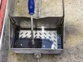 En borste med blått handtag vilar i en vattenfylld smutsavskiljare av metall.
