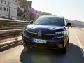 Mörkblå Renault Koleos kör på en bro i solsken. Inga problem syns med bilen.