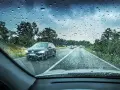 Regndroppar på vindrutan. Bilar kör på en väg genom ett trädbevuxet landskap. Glaco-behandlingen håller sikten klar.