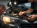 Mekaniker kontrollerar bilens elsystem med multimeter. Halvljuset lyser svagt, vilket tyder på dåligt halvljus.