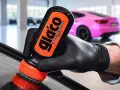 En hand med svart handske applicerar glasförsegling från en Glaco-flaska på en bilruta. En rosa bil syns i bakgrunden.