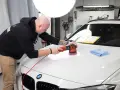 Man polerar en vit bil med en polermaskin, använder Menzerna-produkter för en perfekt finish.