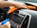 En hand sprayar och torkar av bilens instrumentbräda med en orange trasa. Det ser ut som en magisk rengöring för att få bilen skinande ren.