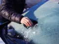 En hand skrapar isfria bilrutor en kall morgon. Snöflingor faller från vindrutan.