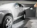 En Kärcher K5 Home skummar upp en mörk SUV. Vatten och skum sprutar över bilen och marken.