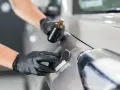 Händer med svarta handskar applicerar keramiskt lackskydd på en ny bil för en glänsande finish.