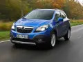 Blå Opel Mokka kör på en väg, kanske med ett opel mokka problem. Träd i höstfärger syns i bakgrunden.