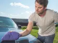 Man puts the finishing touches on his car with a waterless wash, leaving a sparkling shine under a blue sky.