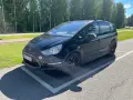 Svart Ford S-Max med takräcke parkerad på en asfalterad yta. En liten bit av stötfångaren verkar vara skadad, ett potentiellt **Ford S-Max problem**.