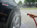 Tvätta bilen hemma medel. Vatten sprutar på en svart GTI-bil.