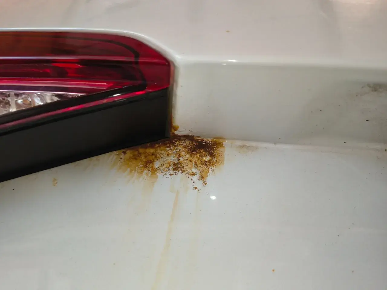 Rostfläckar vid bakljuset på en vit bil. Dags att laga rost bil innan det blir värre.