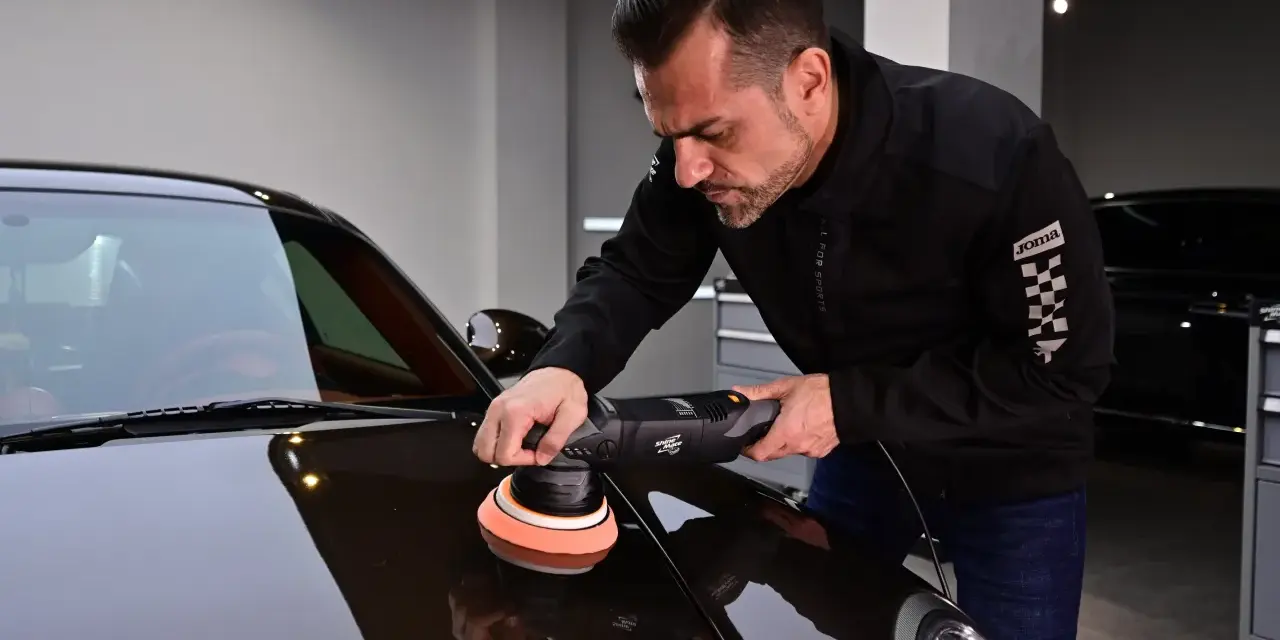 Man polerar en mörk bil med en polermaskin. Autosol ger glans åt lacken.