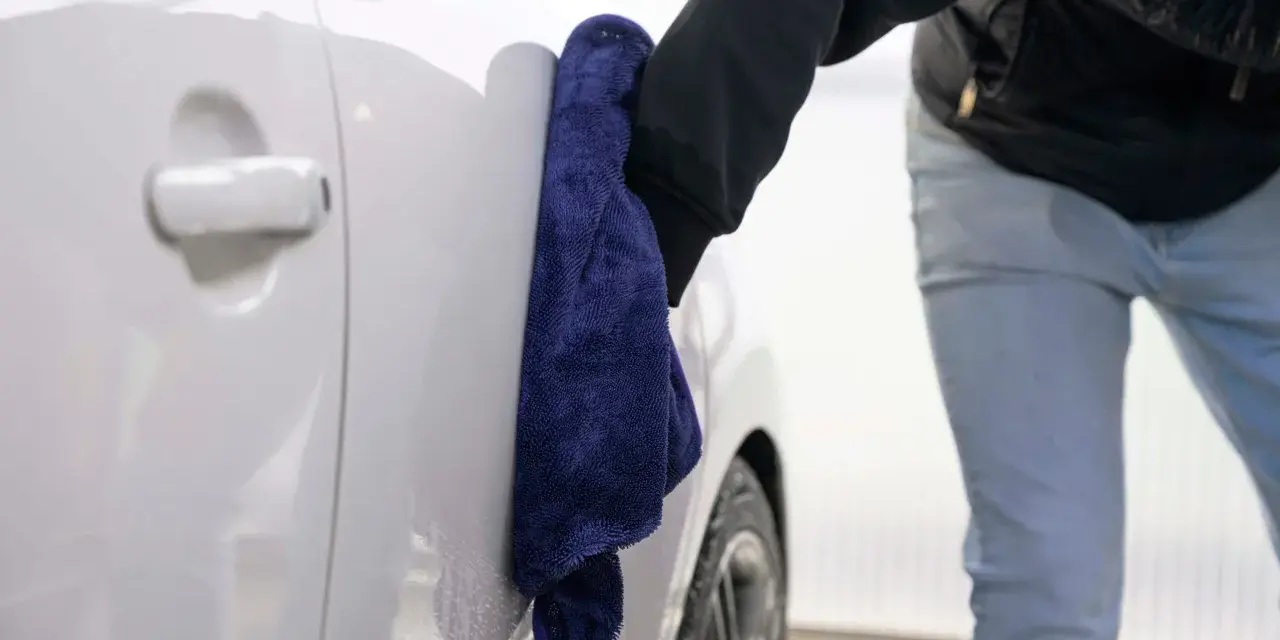 En hand med en mörkblå mikrofiberduk torkar av en vit bil. Super foam ger en glänsande finish.