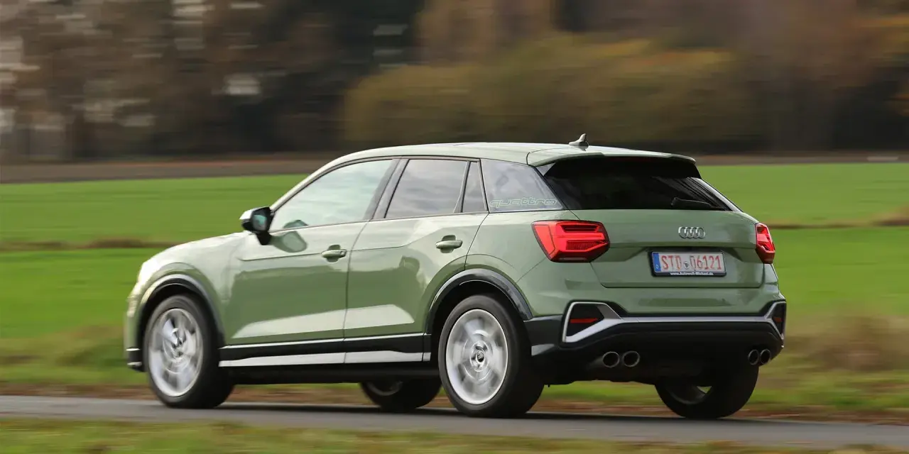 Grön Audi Q2 kör på en landsväg, med suddiga träd och fält i bakgrunden. Kanske ett audi q2 problem med att den kör för fort?
