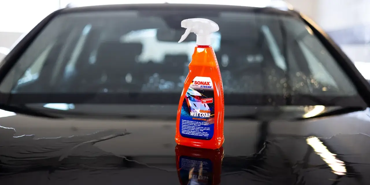 En flaska SONAX Xtreme Ceramic Wet Coat står på en våt bilhuv.