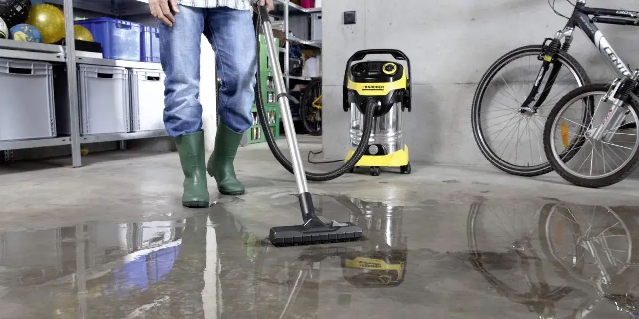 Man i gröna stövlar använder Kärcher WD 6 P Premium för att suga upp vatten på ett betonggolv i ett garage.