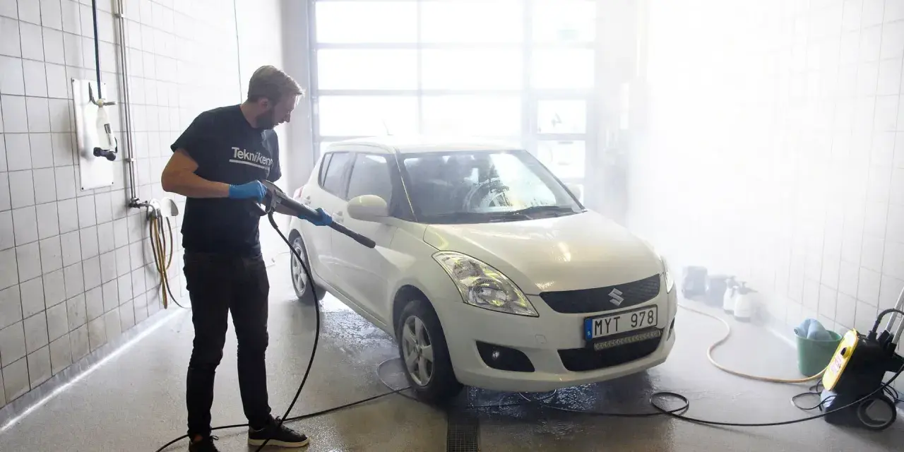 Man med högtryckstvätt gör bilen skinande ren. En riktig asfaltslösare som får bort all smuts.
