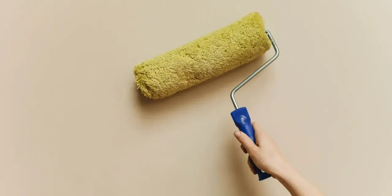 En hand håller en färgroller med gul päls, redo att måla en vägg. Kanske är det dags för en 3m rubbing för att fräscha upp hemmet.