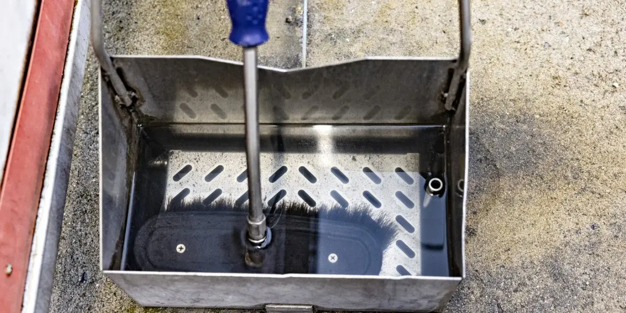 En borste med blått handtag vilar i en vattenfylld smutsavskiljare av metall.