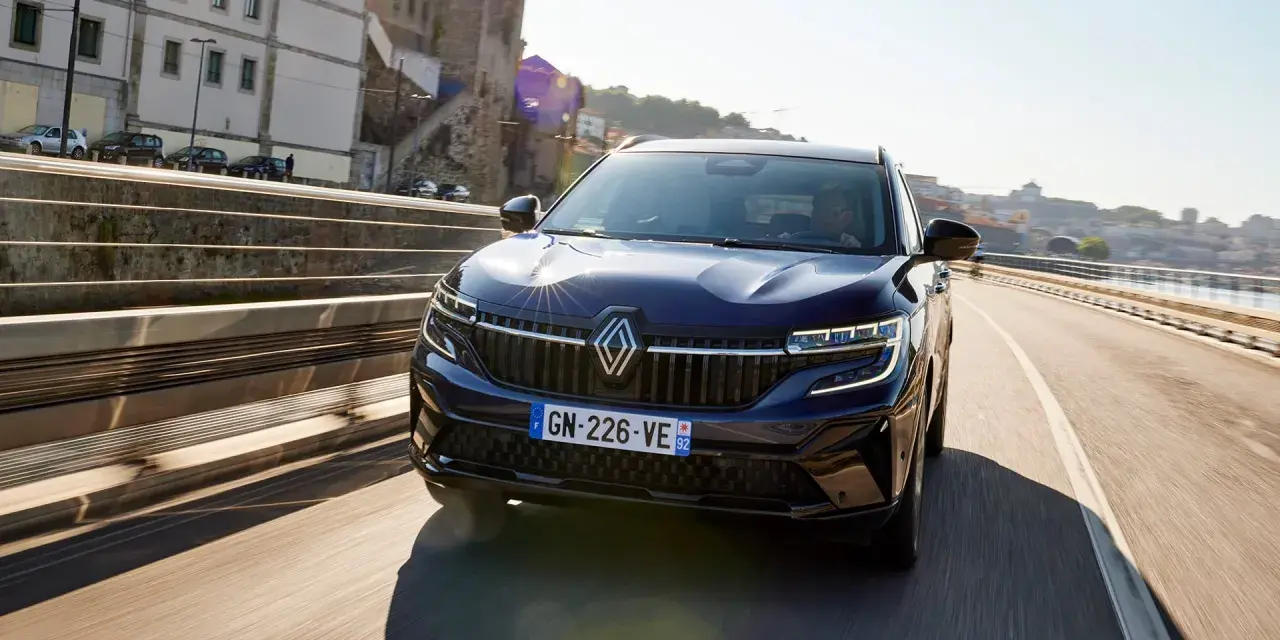 Mörkblå Renault Koleos kör på en bro i solsken. Inga problem syns med bilen.