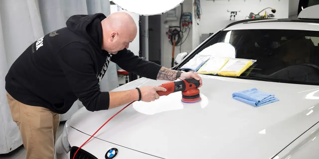 Man polerar en vit bil med en polermaskin, använder Menzerna-produkter för en perfekt finish.