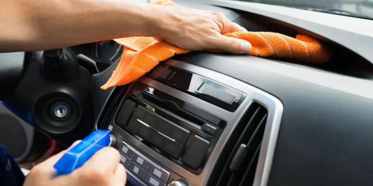 En hand sprayar och torkar av bilens instrumentbräda med en orange trasa. Det ser ut som en magisk rengöring för att få bilen skinande ren.