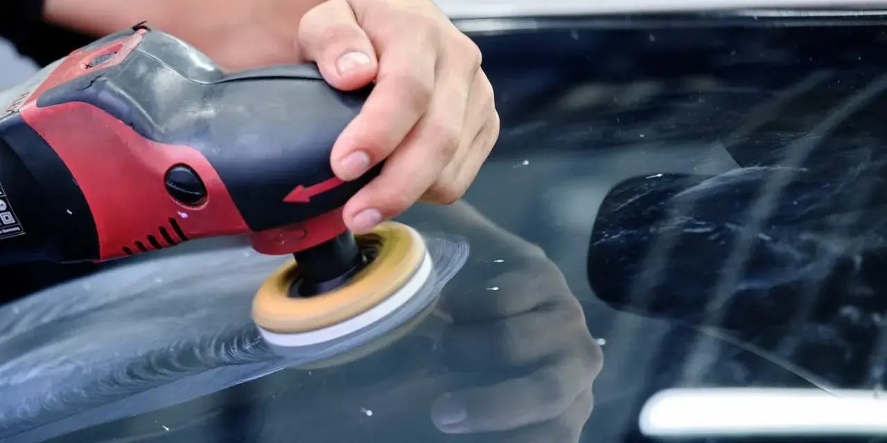 En hand polerar en bilruta med en polermaskin. Glaspolish ger en perfekt finish.