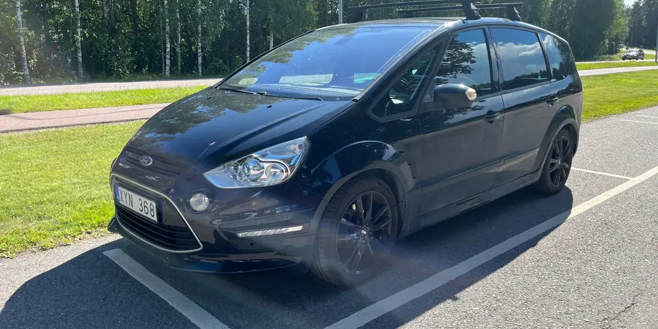 Svart Ford S-Max med takräcke parkerad på en asfalterad yta. En liten bit av stötfångaren verkar vara skadad, ett potentiellt **Ford S-Max problem**.