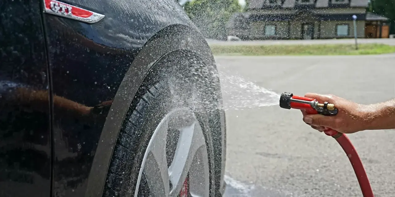 Tvätta bilen hemma medel. Vatten sprutar på en svart GTI-bil.