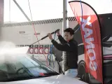 Man using a pressure washer on a car windshield, with a SONAX banner in the background.