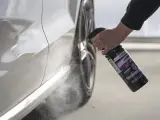 En hand sprutar Sonax kallavfettning på en vit bil.