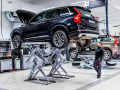 Mekaniker arbetar med en svart Volvo på en billyft i en auktoriserad verkstad.