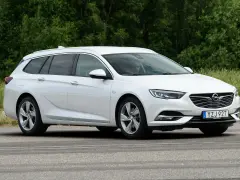 Vit Opel Insignia kombi parkerad vid en grönskande skog. En förare syns i bilen, kanske funderar på ett opel insignia problem.