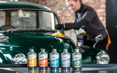 En kvinna polerar en grön bil med en maskin. Framför bilen står fem flaskor med bilvårdsprodukter, redo att vaxa bilen.