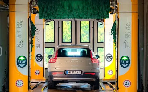Volvo XC40 i en automatisk biltvätt med autoclean + wax-program. Gröna borstar hänger redo för en skinande ren bil.