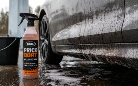 En flaska med MAC Prick Bort kallavfettning står bredvid en smutsig bil. Denna produkt är perfekt för att få bort asfalt, tjära och olja, vilket ger en renare bil.