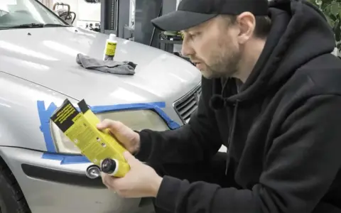 Man förbereder polering strålkastare biltema. En flaska med produkt och trasa ligger på bilen.