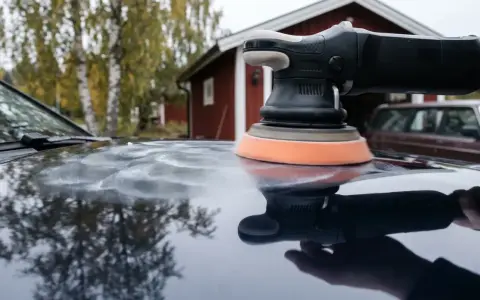 Polermaskin med skumrondell skapar virvlar på bilens lack. I bakgrunden syns ett rött hus och en äldre bil.