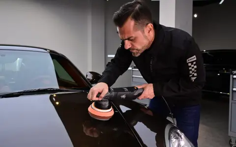 Man polerar en mörk bil med en polermaskin. Autosol ger glans åt lacken.